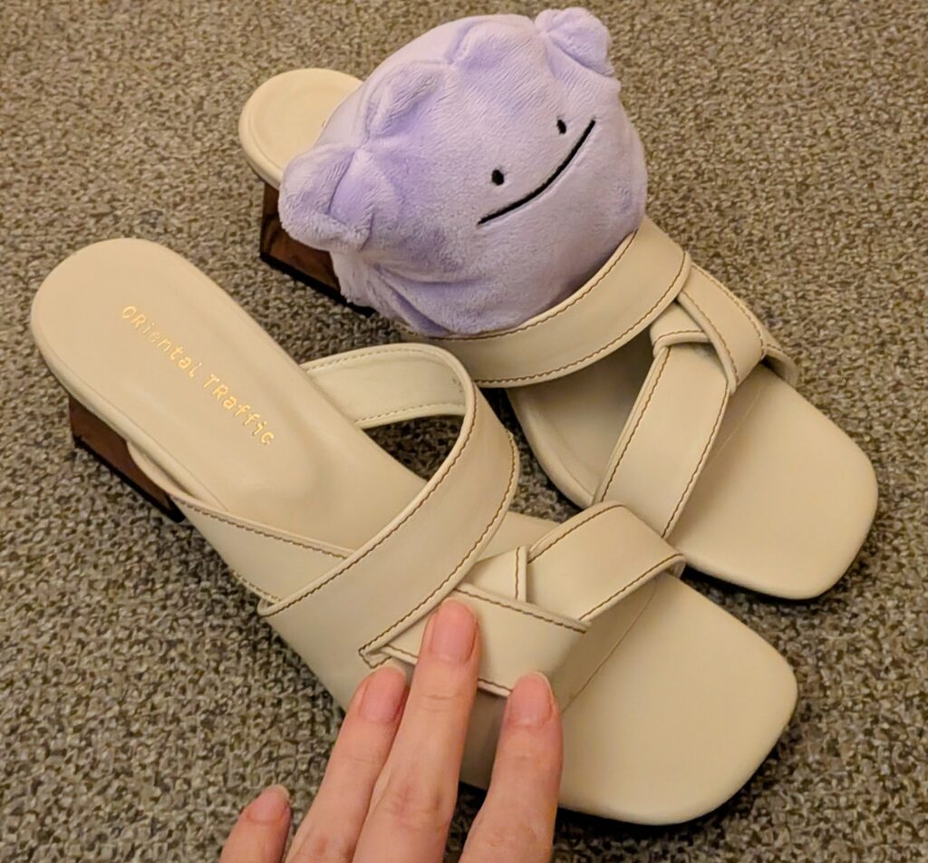 ダブルエーの優待品「ウッドヒールクロスリボンサンダル」のベージュと、その上に乗るメタモンのぬいぐるみ